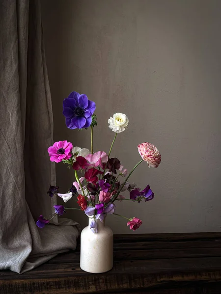 Beautiful flowers in vase on moody rustic background. Stylish flowers still life, artistic composition of lathyrus, anemone, ranunculus. Floral vertical wallpaper