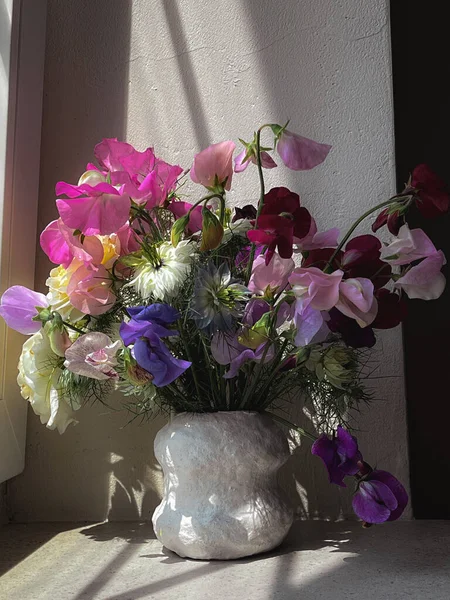 Beautiful flowers in vase on moody rustic background. Stylish flowers still life, artistic composition of lathyrus, love in the mist, rose. Floral vertical wallpaper