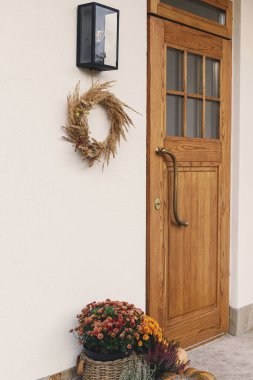 Sonbahar kır çelenkleri, balkabakları ve çiçek saksıları ahşap ön kapıda. Çiftlik evinin girişi ya da verandasının sonbahar dekoru. Sonbahar düzenlemesi