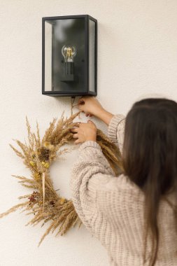 Sonbahar çelengi tutan örgü kazaklı bir kadın ve dekorasyon evi girişi. Kırsal sonbahar çelengi, kurutulmuş çimenler ve çiftlik evinin ön kapısı için böğürtlenler.