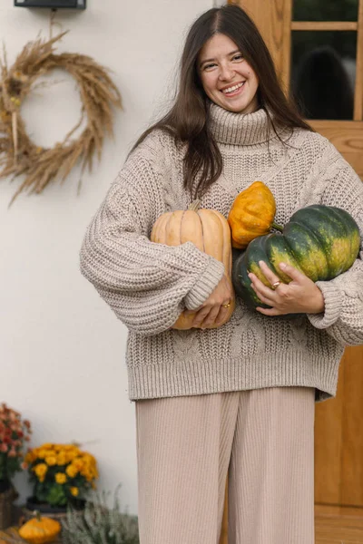 家の入り口の装飾のための大きい秋のカボチャを握る編まれたセーターの幸せな女性 ファームハウスの玄関を飾るスタイリッシュな女性 フォールアレンジメント — ストック写真