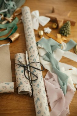 Noel hediyesini paketliyorum. Şenlikli ambalaj kağıdı, makas, kurdele ve ahşap masa üzerindeki modern dekorasyonlar. Mutlu Noeller ve mutlu tatiller!