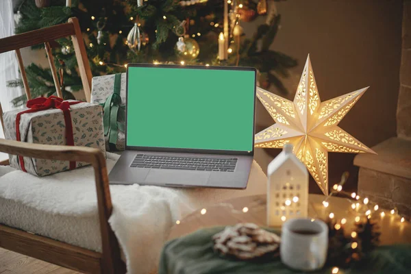 圣诞节网上购物和销售 在装饰着树木 金色灯光和星星的喜庆房间里 配有空屏幕的笔记本电脑和时髦的圣诞礼物放在现代椅子上 笔记本电脑模拟 复制空间 — 图库照片