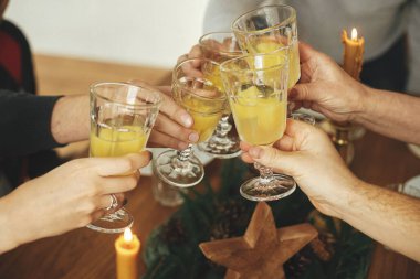 Mimoza kokteyli bardaklı eller Noel masasının arka planına tıklayarak köknar dalları, çam kozalakları ve mumlarla donatılmış. Arkadaşlar ve aile şampanyayla kutlama ve kadeh kaldırma