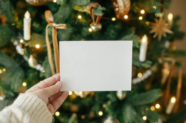 Altın ışıklarla süslenmiş şık Noel ağacının arka planında el ele tutuşan boş tebrik kartı. Noel kartı maketi. Mesaj için yer var. Season selamlama şablonu