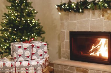 Şık paketlenmiş Noel hediyeleri, şenlikli ışıklandırmalı Noel ağacı ve yanan şömine. Atmosferik Noel arifesi, tatil zamanı. Mutlu Noeller.!