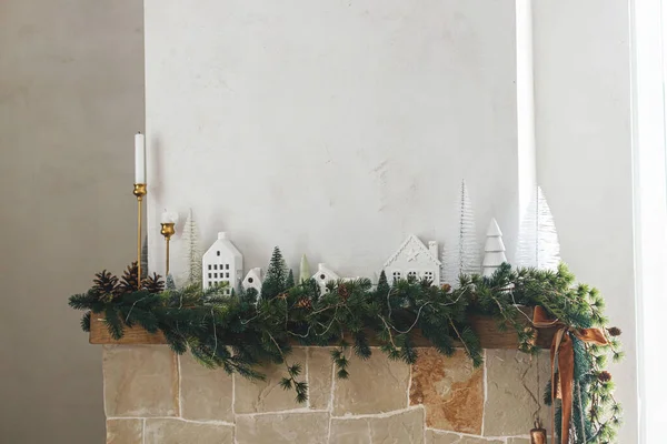 スタイリッシュな装飾されたクリスマスの暖炉 現代のクリスマスツリー 松のコーン 真鍮の鐘とリボンが付いている暖炉のマントルの枝 クリスマスのスカンジナビアのリビングルームの装飾 — ストック写真