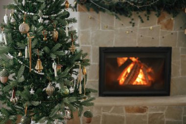 Yanan şömineye karşı şık bir Noel ağacı. Çok güzel dekore edilmiş bir Noel ağacı. Şöminenin arka planında eski incik boncuklar ve kurdeleler var. Atmosferik Noel arifesi. Mutlu Noeller.!