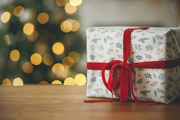 别致的圣诞礼物在树灯的映衬下紧贴在一起 圣诞快乐 木制桌子上有红丝带的漂亮的现代包装礼物 圣诞背景 复制空间 — 图库照片