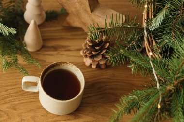 Kış tatili iksiri. Şık bir fincan sıcak çay, sepetteki köknar dalları, tahta ağaçlar ve yıldız, kozalaklar ve masa ışıkları. İskandinav odasında modern noel kırsal çevre dostu dekor