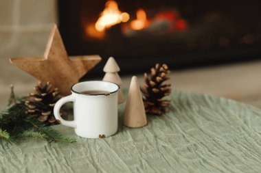 Şık bir fincan sıcak çay, köknar dalları, tahta ağaçlar ve yıldız, şöminenin karşısında duran kozalaklar. Modern Noel rustik çevre dostu dekor ve boş kupa, İskandinav kış ikilisi