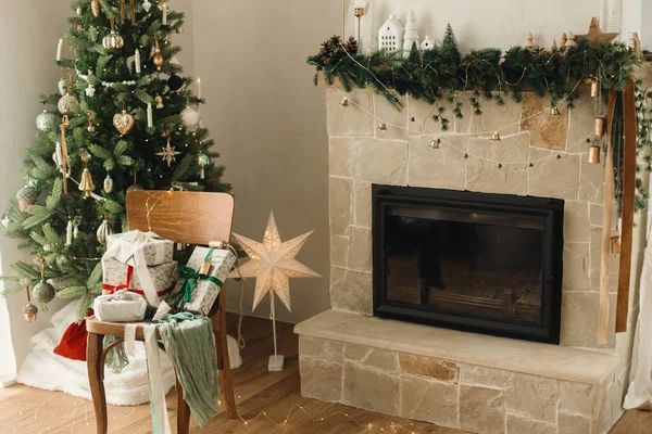 メリークリスマスとハッピーホリデー 現代装飾されたクリスマスツリーとお祝いのライトと素朴な暖炉の背景に木製の古い椅子にリボンが付いているスタイリッシュな包まれたクリスマスギフト — ストック写真