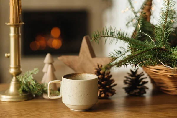 コージーウィンター 暖かいお茶のスタイリッシュなカップ 火の枝 木の木 火の暖炉に対するテーブルの上の松のコーン 現代クリスマス素朴なエコフレンドリーな装飾 スカンジナビアの衛生 — ストック写真