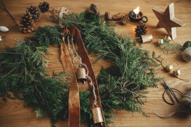 Sedir dalları, kurdele, eski çanlar, çam kozalakları, sicim, ahşap masa üzerinde makas olan şık bir Noel rustik çelengi. Mutlu noeller. Atmosferik odada kış tatili hazırlıkları