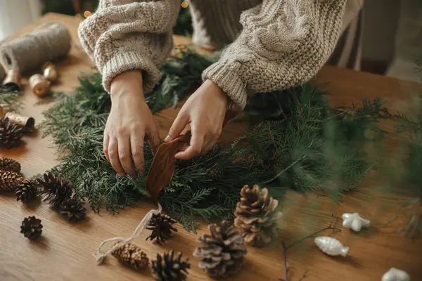 手穿舒适的毛衣 用冷杉枝条 木制桌子上的铃铛做圣诞乡村花环 寒假准备 大气时间 — 图库照片