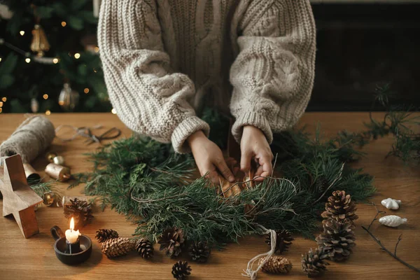 Ręce Przytulnym Swetrze Wykonując Świąteczny Wieniec Gałązkami Jodły Wstążką Szyszkami — Zdjęcie stockowe
