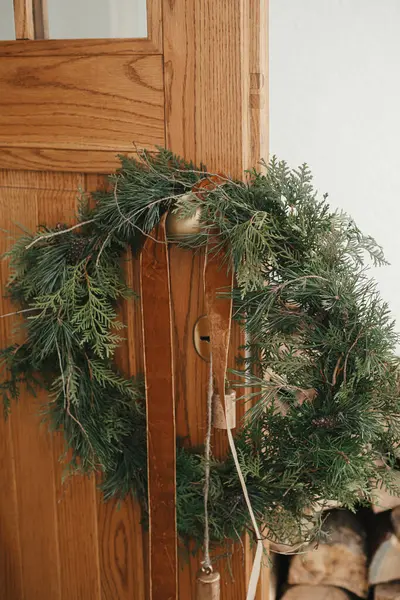 风格别致的圣诞乡村花环 在木门上的黄铜把手上挂着老式铃铛和彩带 冬季度假装饰的现代农舍外入口 圣诞快乐 — 图库照片