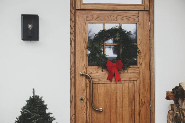 木门上有红色的蝴蝶结 家门口有红色蝴蝶结的冷杉树 现代农舍外部寒假装饰 — 图库照片