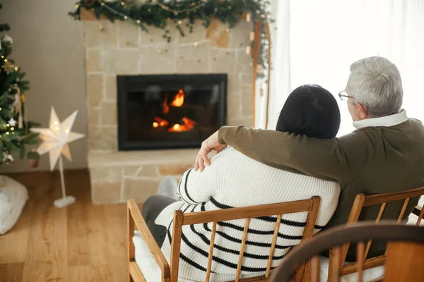 美丽的老夫妇拥抱并享受舒适的壁炉在时尚的圣诞装饰客厅 舒适的冬天 快乐的老年家庭放松 节日快乐 — 图库照片