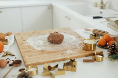 Modern beyaz mutfakta zencefilli kurabiye yapıyorum. Tahtada zencefilli ekmek hamuru, un, merdane, altın metal kesici, mutfak tezgahında yemek pişirme baharatları ve şenlikli süslemeler.