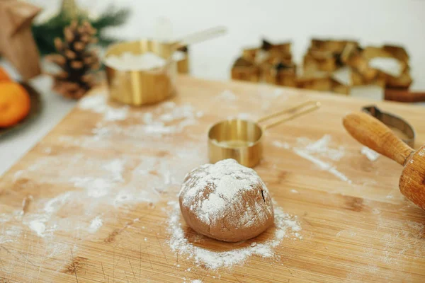 Making christmas gingerbread cookies in modern white kitchen. Gingerbread dough on wooden board, flour, rolling pin, golden metal cutters, cooking spices and festive decorations on countertop