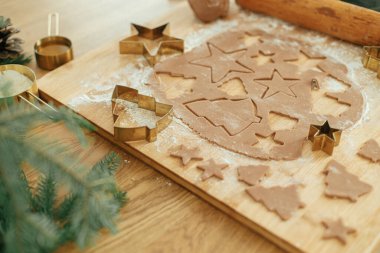 Noel kurabiyesi yapmak, atmosferik tatil zamanı. Altın kesicili zencefilli hamur, merdane, köknar dalları ve sade ahşap masa üzerindeki şenlikli süslemeler