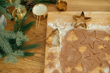 Noel kurabiyelerini düzleştirmek, atmosferik tatil zamanı. Altın kesicili zencefilli hamur, merdane, köknar dalları ve sade ahşap masa üzerindeki şenlikli süslemeler