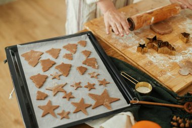 Çiğ zencefilli kurabiyeler, bayram süslemeleri ile birlikte kırsal masada pişirme tepsisinde. Kadın Noel kurabiyesi yapıyor, atmosferik tatil zamanı.