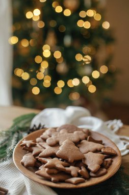 Mutlu Noeller! Noel kurabiyeleri ahşap tabakta kırsal masada, Noel 'in altın ışıklarının arka planında. Lezzetli zencefilli kurabiyeler, atmosferik tatil