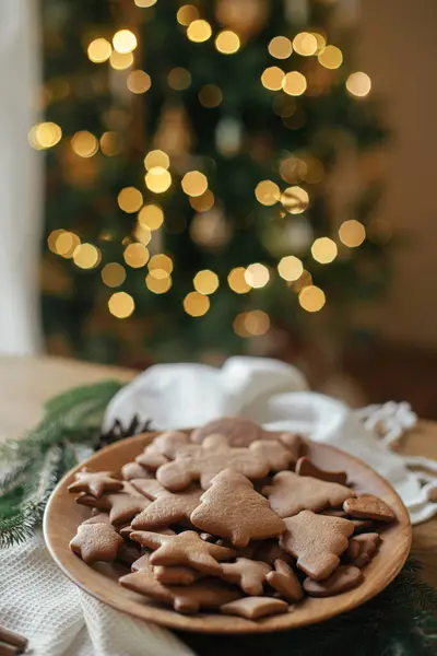 Mutlu Noeller! Noel kurabiyeleri ahşap tabakta kırsal masada, Noel 'in altın ışıklarının arka planında. Lezzetli zencefilli kurabiyeler, atmosferik tatil