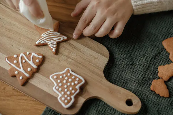 素朴な木製テーブルの上にアイシングでジンジャーブレッドクッキーを飾る 大気のクリスマス休日の伝統 砂糖フロスティングで焼いたクリスマスクッキーを飾る手 ファミリータイム — ストック写真