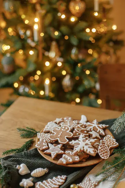 クリスマスジンジャーブレッドクッキー お祝いの素朴なテーブルに金色のイルミネーションに対する装飾とプレートでアイシング メリークリスマス おいしいジンジャーブレッドクッキー 大気の休日のイブ — ストック写真