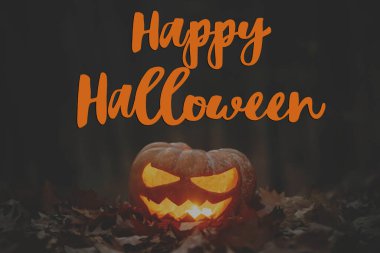 Mutlu Cadılar Bayramı! Cadılar Bayramı mesajın kutlu olsun ve kasvetli karanlık ormandaki sonbahar yapraklarında parlayan ürkütücü Jack o fener. Korkunç atmosferik Cadılar Bayramı tebrik kartı, el yazısı.