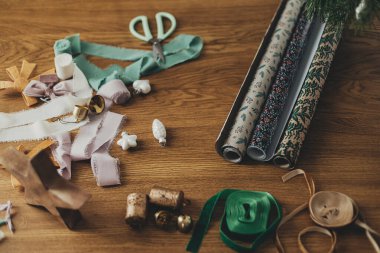 Şık Noel ambalaj kağıtları, kurdeleler, makas, yıldız ve pirinç çanlar arka plandaki ahşap masada. Noel hediyelerini paketliyorum. Kış tatili hazırlığı, üst manzara