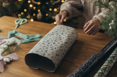 Noel hediyelerini paketliyorum. Ellerin rahat süveter içinde şık bir hediye paketinin içinde kurdelelerle, eski süslemelerle, ahşap masanın üzerinde fiyonklarla. Atmosferik kış tatili