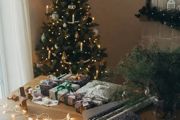 クリスマスプレゼントのラッピング スタイリッシュなプレゼント お祝いのラッピングペーパー リボン ハサミ スター 真鍮の鐘クリスマスツリーライトの背景に木のテーブルに 大気の冬の休日 — ストック写真