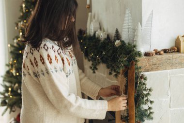 Noel şöminesini kadife kurdeleyle süslüyor ve köknar dallarında eski çanlar çalıyor. Modern çiftlik evindeki şömine rafına hoş süveterli bir kadın asılmış. Atmosferik kış tatili