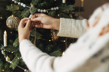 Noel ağacını şık bir kurdeleyle süslemek. Konforlu kazaklı bir kadın ağaç dalına modern kadife süslemeler asıyor. Atmosferik kış tatili geleneği, aile zamanı