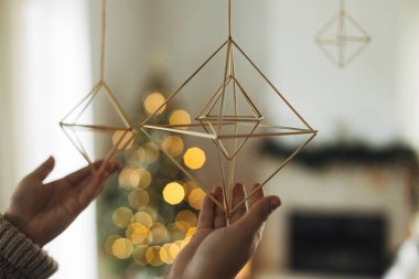 Eller rahat süveter giyip arka planda modern çiftlik evinin oturma odasında şenlikli altın ışıkların üzerine saman saman süslemesi asıyor. Evi Noel saman örümcekleriyle süslemek.