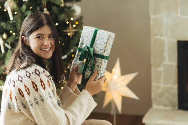 穿着舒适毛衣的女人拿着时尚的圣诞礼物 背景是装饰过的圣诞树 客厅里点着灯 大气寒假时间 准备圣诞礼物 — 图库照片