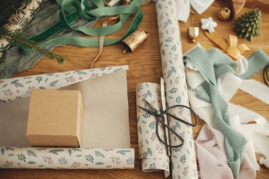 Noel hediyesini paketliyorum. Şenlikli ambalaj kağıdı, el işi hediye kutusu, makas, kurdeleler ve ahşap masa üzerindeki modern dekorasyonlar. Mutlu Noeller ve mutlu tatiller!