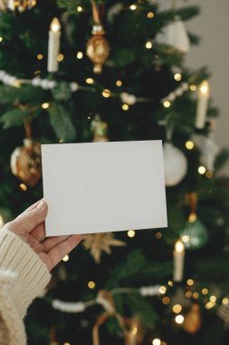 Altın ışıklarla süslenmiş şık Noel ağacının arka planında el ele tutuşan boş tebrik kartı. Noel kartı maketi. Mesaj için yer var. Season selamlama şablonu