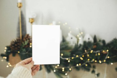 Noel evlerinin arka planında el ele tutuşan boş tebrik kartı, altın ışıklı köknar dalları ve ağaç süslemeleri. Noel kartı maketi. Mesaj için yer var. Season selamlama şablonu