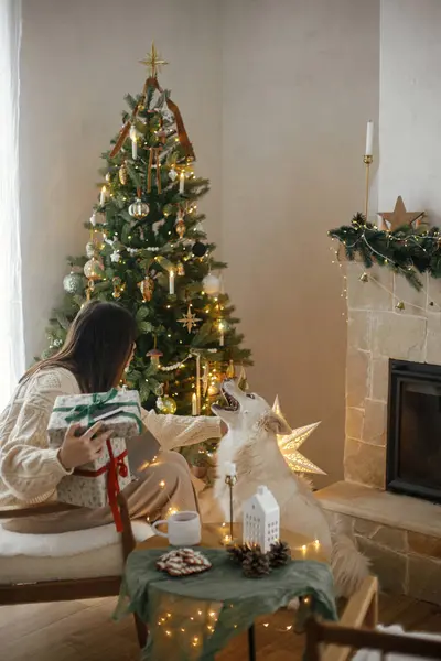 快乐的女人拿着有信用卡的时髦圣诞礼物 在装饰有彩灯的圣诞房间里爱抚可爱的白狗 圣诞网上购物和黑色星期五销售 — 图库照片