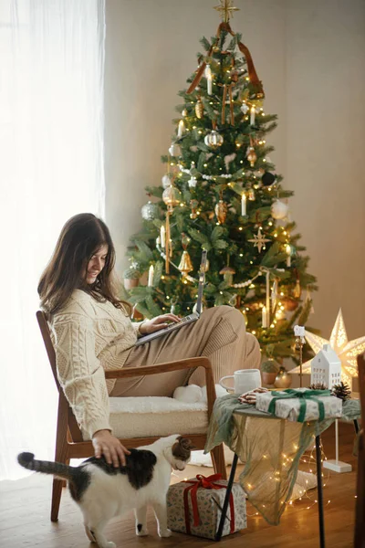 ハッピーな女性は ラップトップで作業し お祝いの飾られたクリスマスルームでかわいい小さな猫を世話します クリスマス休暇とペット 冬休みのリモートワーク — ストック写真
