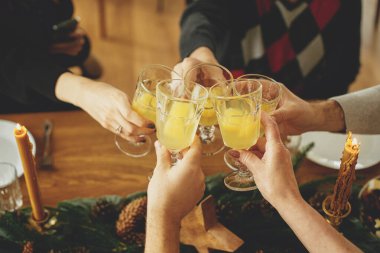Arkadaşlar ve aile kutlama yapıyor ve şampanyayla kadeh kaldırıyor. Mimoza kokteyli bardaklı eller köknar dalları, çam kozalakları ve mumlarla süslü Noel masasının arka planına tıklıyor.