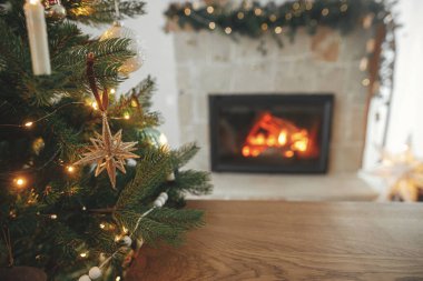Işıklı ve yanan şömineli Noel ağacına karşı ahşap masa. Noel şablonu ve ahşap tahta ürün için hazırlanıyor. Noel arkaplanı, kopyalama alanı