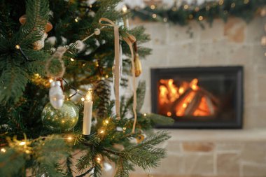 Noel süsleri ağaçta, yanan şömineye yakın duruyor. Klasik takılar ve kurdelelerle süslenmiş güzel bir Noel ağacı. Noel atmosferi. Mutlu Noeller.!