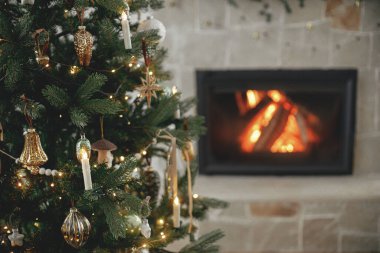 Atmosferik Noel oturma odasında şık bir ağaç ve şömine var. Şenlikli şöminenin arka planında eski püskü mücevherler ve ışıklarla süslenmiş Noel ağacı. Mutlu Noeller.!