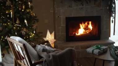 Atmosferik Noel arifesi şöminede. Şık Noel hediyeleri, altın ışıklarla süslenmiş Noel ağacı ve yanan şöminede rahat bir sandalye. Kış kızarıklığı.